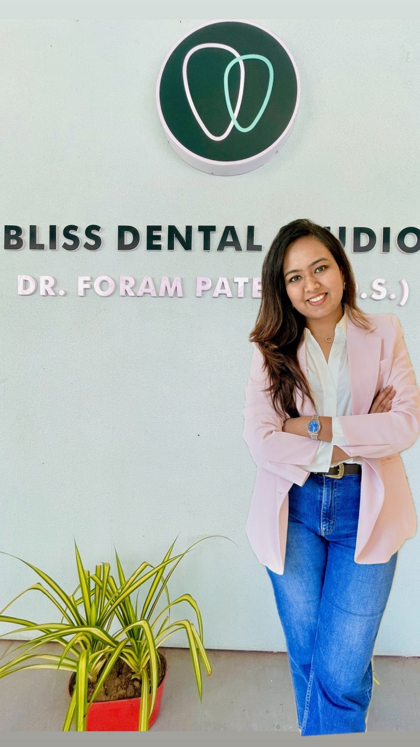 Dr. Foram Patel in a pink blazer beside the Bliss Dental Studio sign